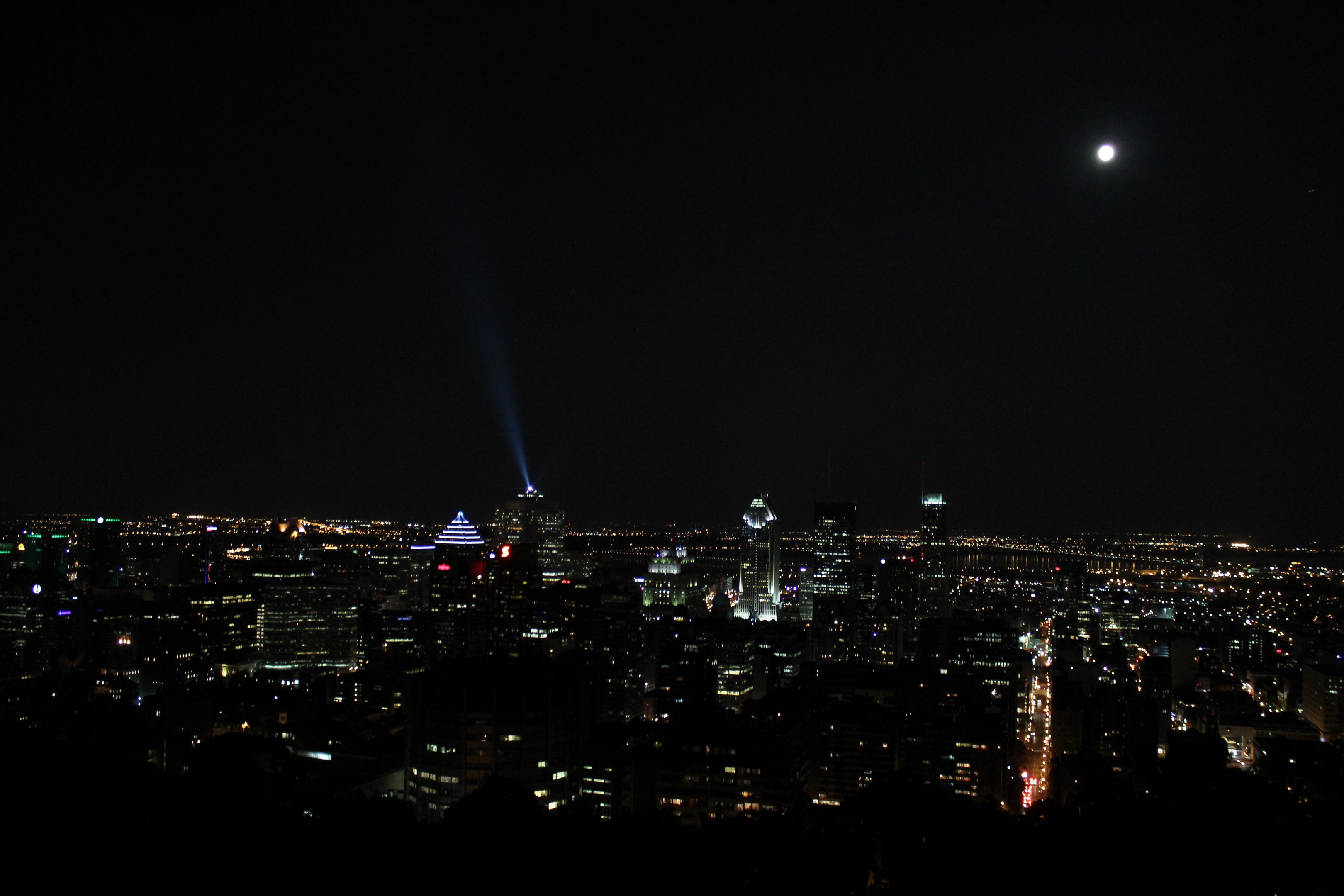 Une ligne d'horizon urbaine la nuit avec des gratte-ciel illuminés, un faisceau lumineux et la pleine lune dans un ciel sombre
