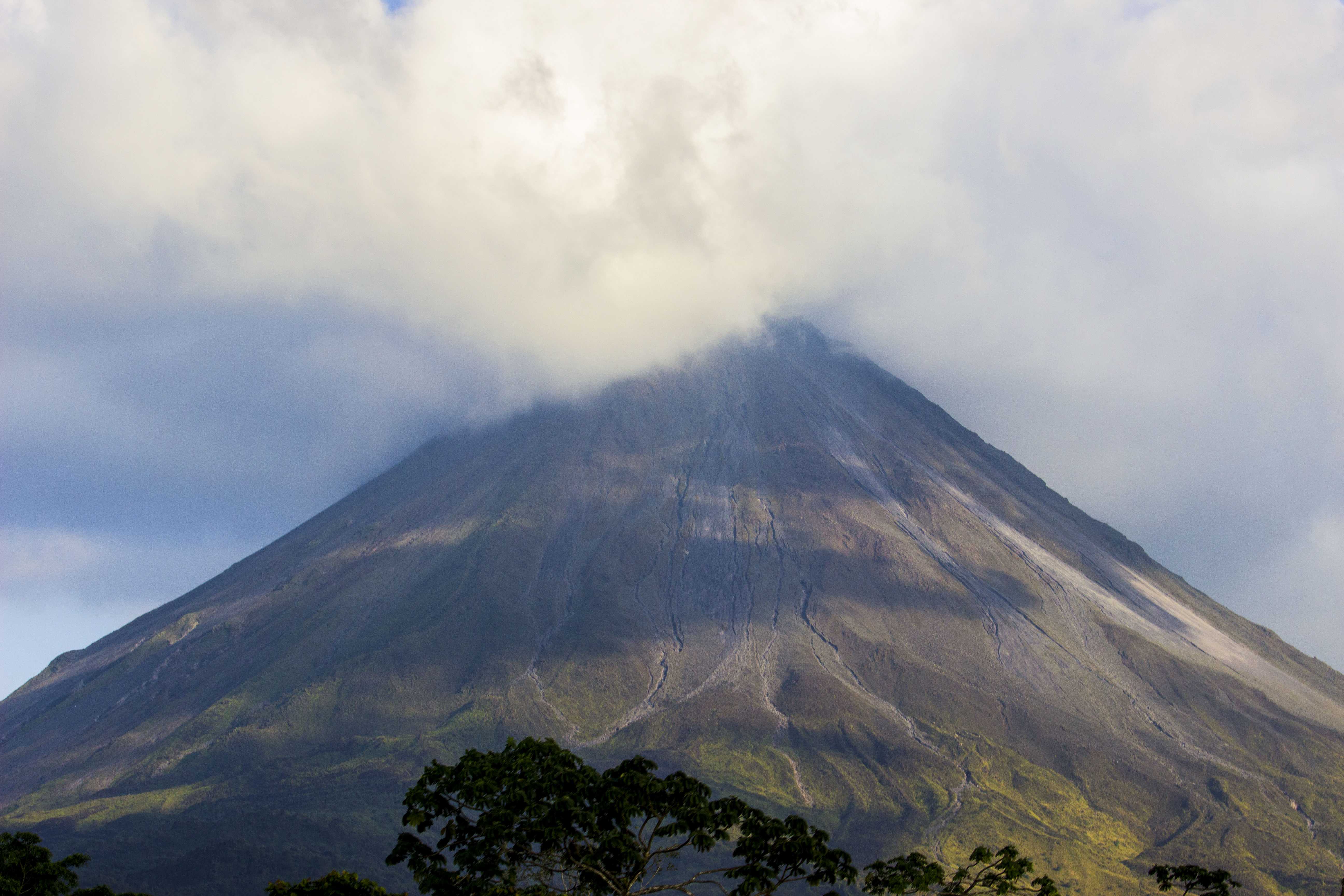 Grand sommet conique partiellement enveloppé de nuages, végétation verte sur les pentes inférieures, évoquant les montagnes d'Asie
